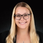 woman wearing glasses, smiling, standing in front of a black backdrop. 