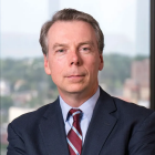 man wearing businesss suit, standing in front of a window. 