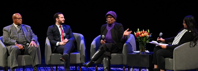 group of people seated on a stage, holding a discussion. 