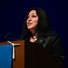 woman standing at podium, speaking.