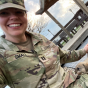 woman in military clothing with puppy chewing on shirt. 