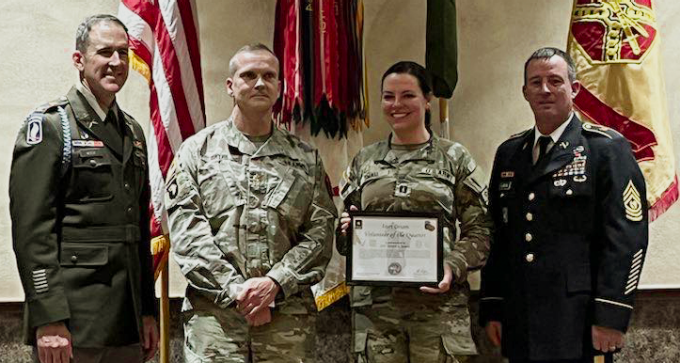 group of military people standing in front of flags, one holding up a certificate. 