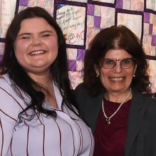Two women standing together, smiling. 