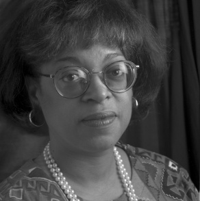 black and white photo of a woman wearing glasses, pearl necklace. 