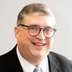 man wearing glasses and suit, smiling. 
