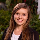 Woman standing outside wearing a black suit, smiling. 