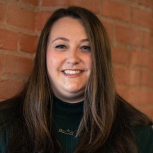 Woman standing in front of a brick wall, smiling. 