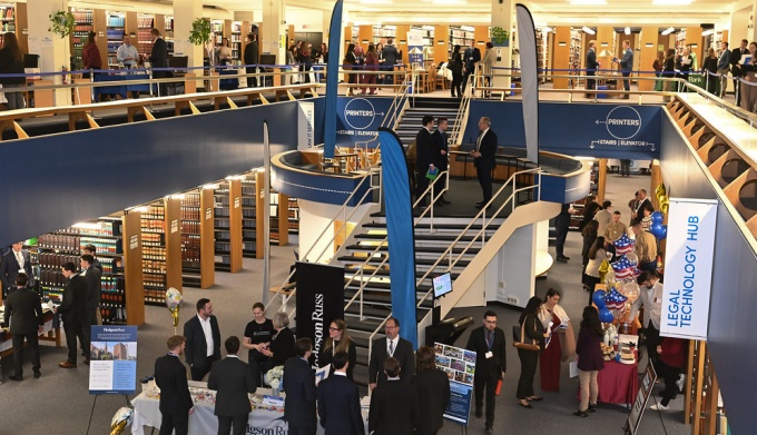 Large atrium for a library, many people standing around tables, talking. 