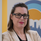 Woman wearing glasses, standing in front of a mural. 
