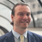 Smiling man standing in the lobby of a building, wearing yellow tie and business grey suit. 