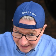 Closeup image of Mac Donald wearing backwards baseball cap that includes text that says Rally On. 