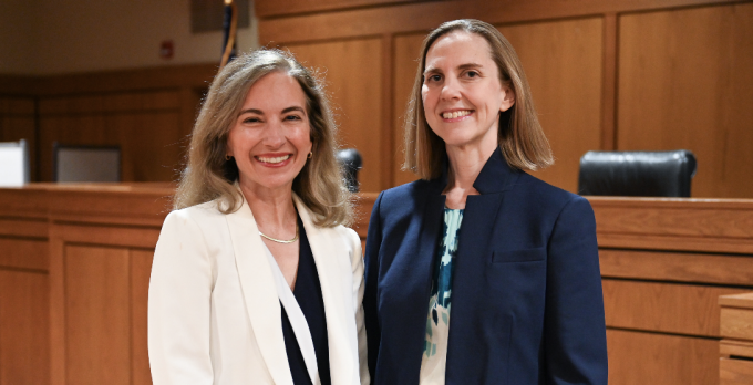 Two women standing in a courtroom, smiling. 