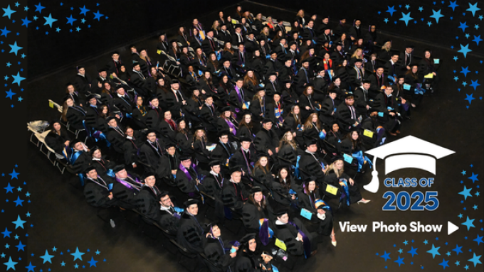 A room full of graduating law students sitting in chairs, lined up, looking up at the camera. 