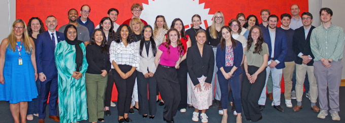 Group of people standing together, smiling, in front of a large red sign that says Mattel. 