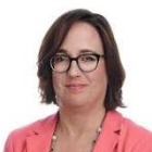 Person wearing a coral-colored blazer over a black top with a beaded necklace, posed against a plain white background in a professional headshot style. 