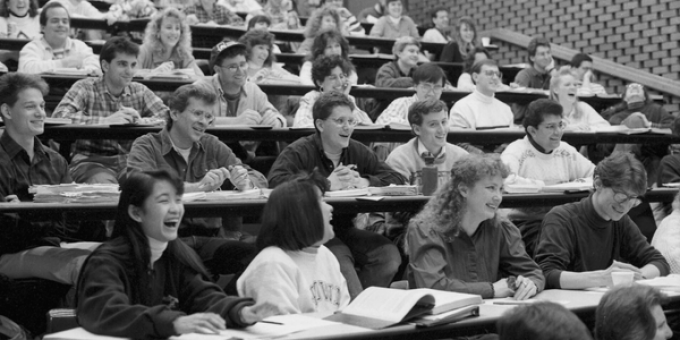 A circa 1980s black and white photo of a classroom with students, smiling and laughing. 