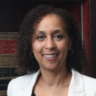 Hon. Trini Ross wearing white jacket, standing in front of a bookshelf of legal books. 