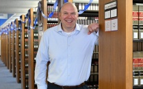 Brian Detweiler posing in the law library among rows of legal reference books decorated with blue streamers. 