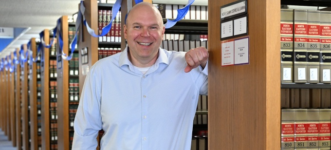 Brian Detweiler posing in the law library among rows of legal reference books decorated with blue streamers. 