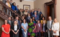 Group portrait of approximately 30 people posed on and around a grand wooden staircase inside a historic building with dark wood paneling and patterned carpeting. 