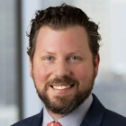 Professional portrait of Gleason wearing red tie, dark blazer jacket.