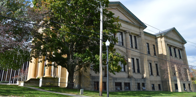 Stone building with columns and large windows, partially shaded by trees. 
