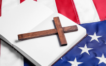 A wooden cross rests on an open book placed on top of an American flag. 