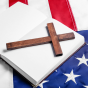 A wooden cross rests on an open book placed on top of an American flag. 