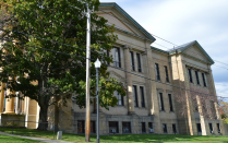 Stone building with columns and large windows, partially shaded by trees. 