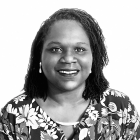 Black and white headshot of a person wearing a floral patterned top, facing the camera against a light background. 