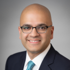 A head‑and‑shoulders professional portrait of an individual wearing a dark blazer, white shirt and green tie. 