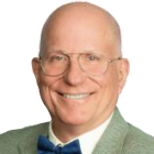 Professional headshot of a person wearing glasses, a light green blazer, and a blue bow tie against a plain background. 