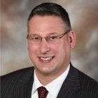 A head‑and‑shoulders professional portrait of an individual wearing a dark blazer, white shirt and tie. 