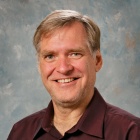 Portrait of Stephen Paskey wearing a long sleeve button down shirt, photographed against a neutral studio background. 