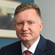 man wearing a business suit, red tie, in an office with a blue wall. 