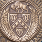 Partial close up of a bronze University at Buffalo seal featuring a buffalo and shield design, shown against a solid blue background. 