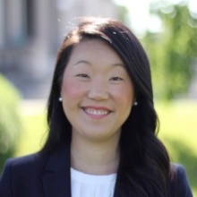 Smiling woman wearing black jacket, white top, standing outside.