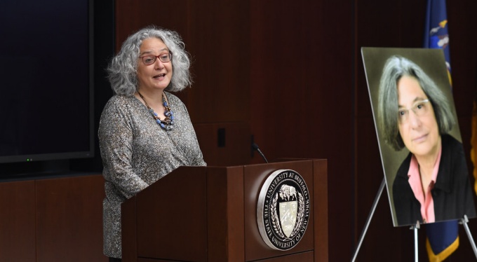 Prof. Bramen speaking at a podium, a large photo of Isabel Marcus is displayed on an easel. 