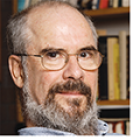 man wearing glasses, sitting in front of a bookshelf. 