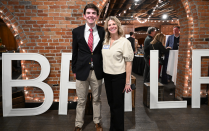 Zoom image: Two attendees stand in front of large illuminated letters and brick archways at an indoor event.