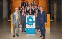 Zoom image: Group of University at Buffalo School of Law community members pose around a UB School of Law "Horns Up!" display inside a campus building.