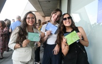 Zoom image: Three attendees hold event cards while posing for a photo at a University at Buffalo School of Law gathering.