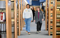 Zoom image: People walking down an aisle in a library, surrounded by tall bookshelves filled with legal volumes.