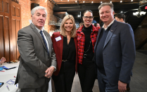 Zoom image: A group of four attendees pose together in a brick-walled event space with string lights overhead.