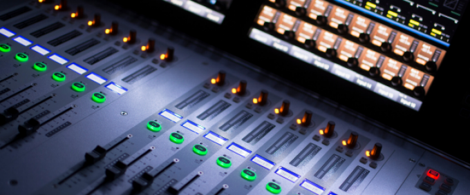 Closeup image of a recording studio mixing board with buttons and sliders. 