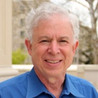 man smiling, standing outside, wearing blue shirt. 