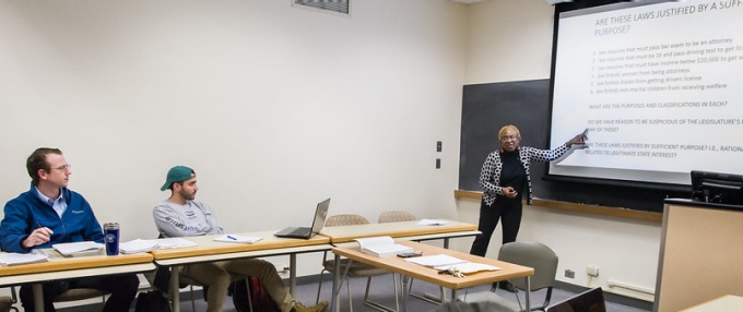 photo of professor mutua teaching a class, pointing at a white board with text written on it. 