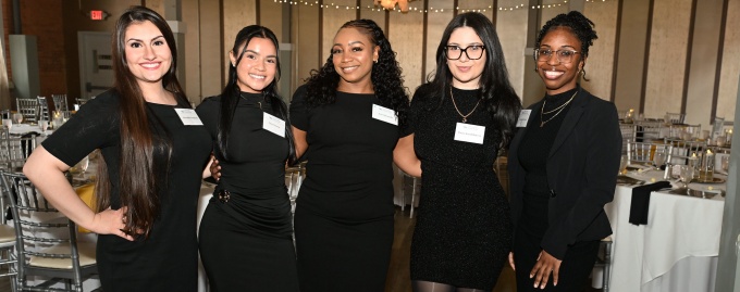 Five law students pose together at a formal student organization event in a banquet hall. 