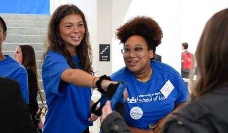 three smiling women handing out materials to students. 